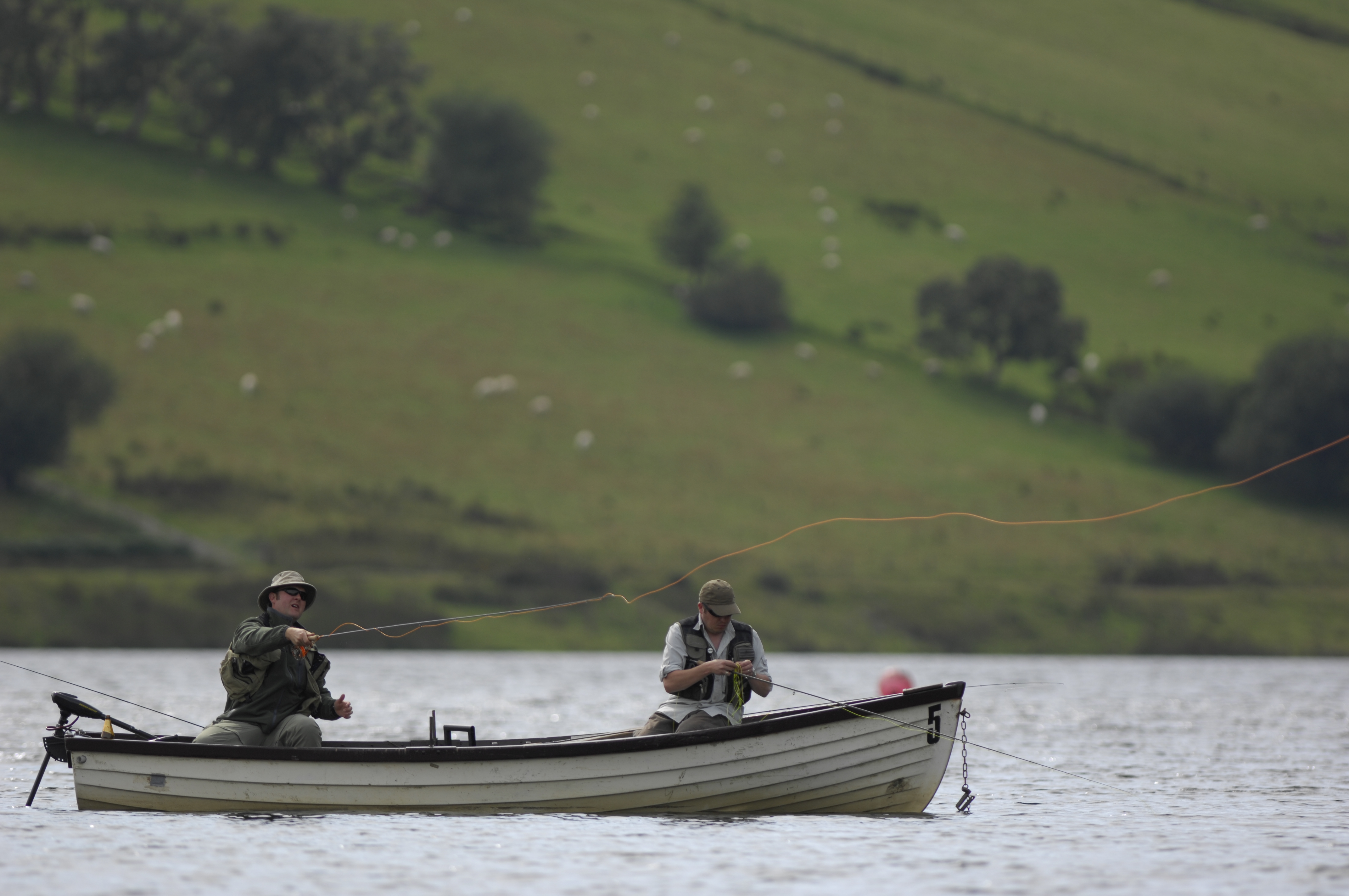 Two men sat in a boat on a river fishing 