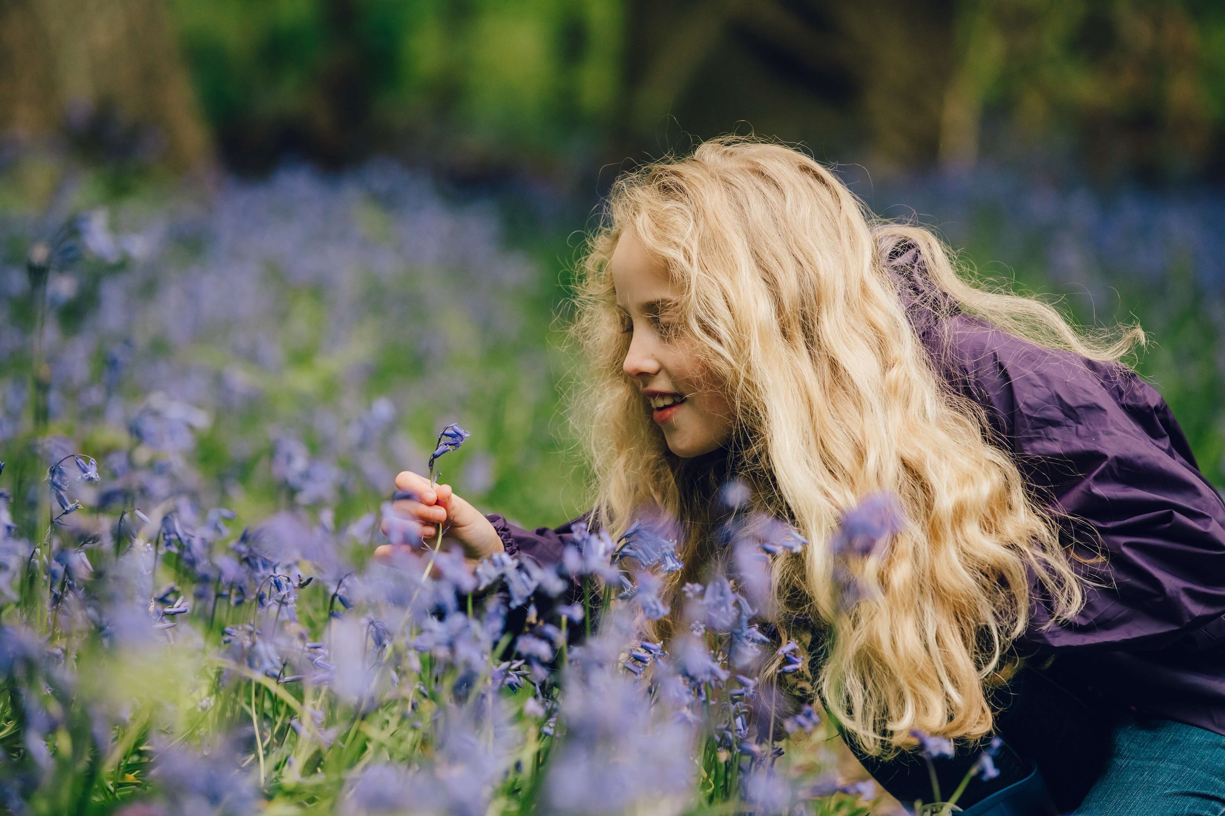 Merch yn edrych ar bluebell yn y coed 
